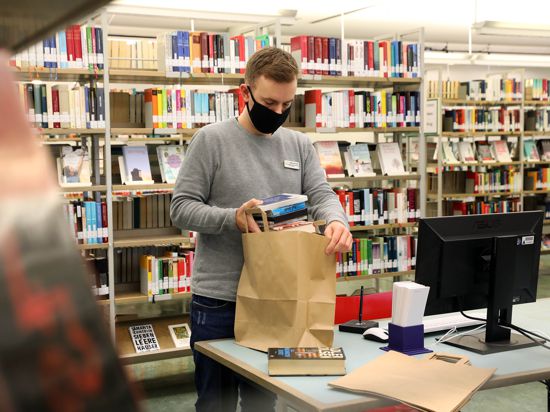 Bibliothekar Jan Roth packt die bestellten Bücher in eine Papiertüte. 