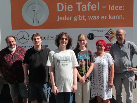 Sechs Menschen stehen vor einem Schild der Karlsruher Tafel.
