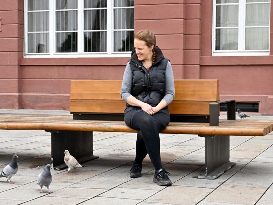 Frau sitzt auf einer Bank vor dem Rathaus und beobachtet Tauben