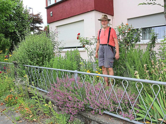 Axel Plitt steht in seinem Wildblumen-Garten in Karlsruhe. Einige Pflanzen ragen über Mauer und Zaun hinaus auf den Gehweg. 