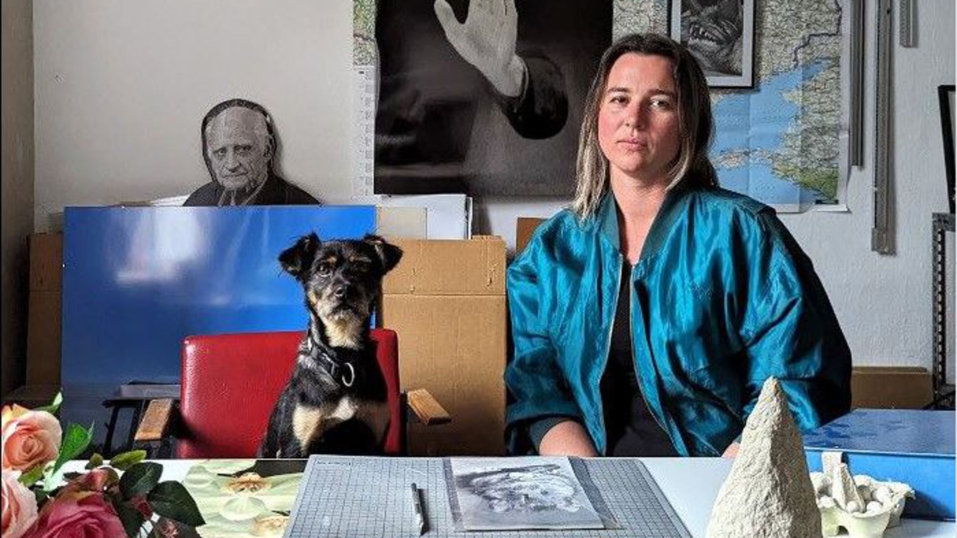 Die Künstlerin Katharina Baumann an einem Tisch mit Kunstwerken neben einem Hund.