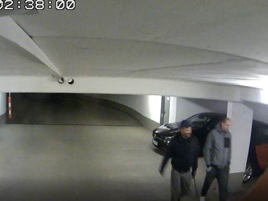 Screenshot einer Videokamera, der zwei Männer in dunkler Kleidung in einer Tiefgarage zeigt.