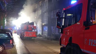 Ein Feuerwehrwagen steht vor einem Gebäude, aus dem Rauch dringt.