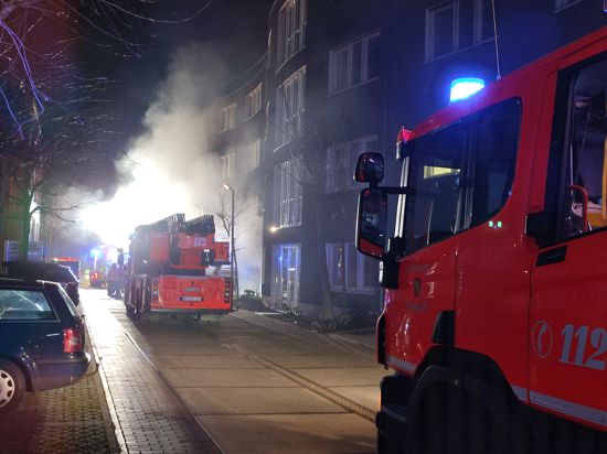 Ein Feuerwehrwagen steht vor einem Gebäude, aus dem Rauch dringt.