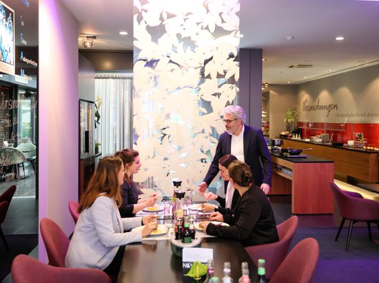 Vier Frauen speisen im Restaurant eines Hotels, der Gastgeber steht neben dem gedeckten Tisch.