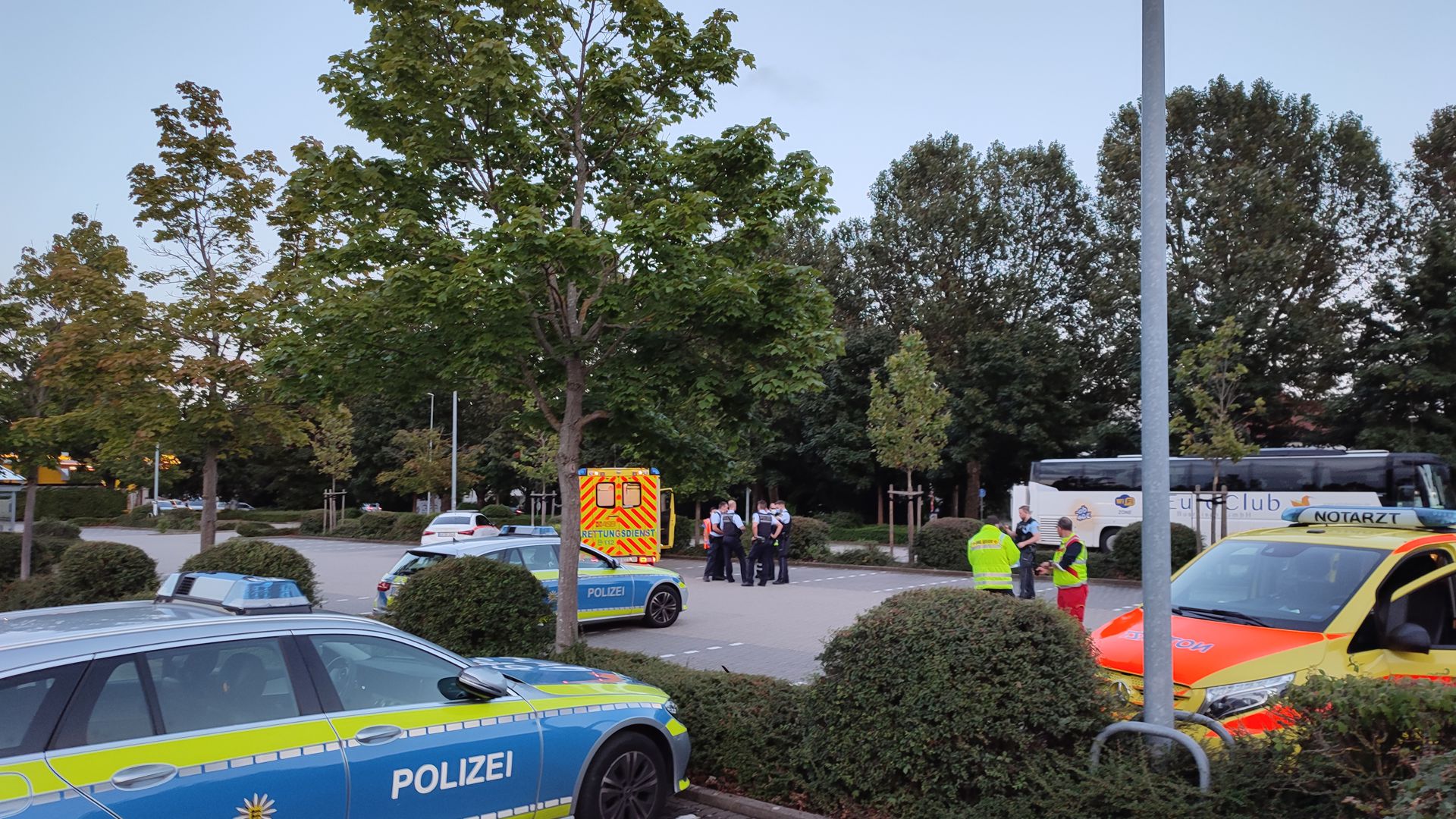 Auf einem Parkplatz befinden sich zwei Rettungswagen, zwei Polizeiautos und eine Gruppe von Polizisten.
