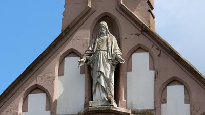 Turmfalke am Fuß der Jesus Skulptur an der Fassade der Kapelle des Bergfriedhofs Durlach