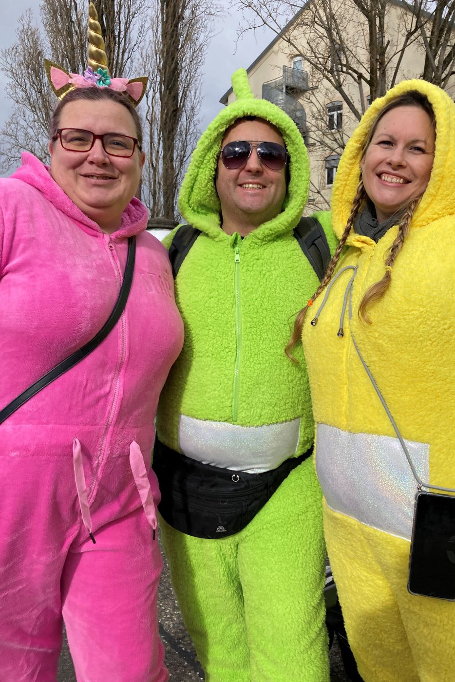 Ein Mann zwischen zwei Frauen, alle drei tragen neonbunte Plüschoveralls