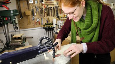 An einer Laubsägemaschine arbeitet eine junge Frau mit Sperrholz.