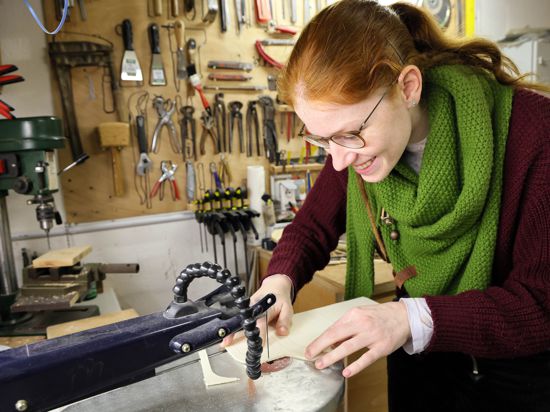 An einer Laubsägemaschine arbeitet eine junge Frau mit Sperrholz.