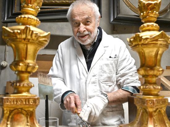 Arno Bettini in seiner Werkstatt. Vor ihm stehen zwei große vergoldete Kerzenständer.