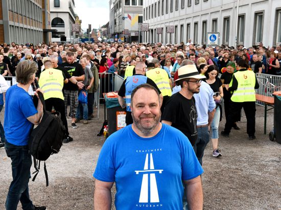 Ein Besucher des Open-Air-Auftritts von Kraftwerk vor dem Karlsruher Schloss steht in einem T-Shirt mit dem Aufdruck „Autobahn“ vor dem Einlass, der gerade erst geöffnet worden ist. Die wartende Menge füllt den Platz der Grundrechte bis zum Zirkel.