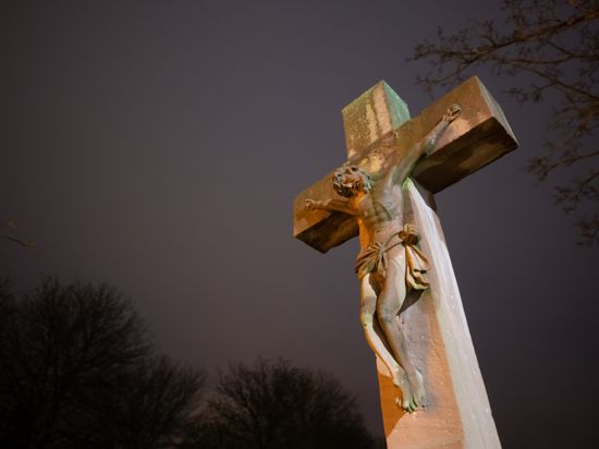 Eine Steinkreuz mit Jesusfigur wird von einem Licht angeleuchtet. Am Karfreitag gedenken Christen an das Leid und das Sterbens Jesu Christi am Kreuz. +++ dpa-Bildfunk +++