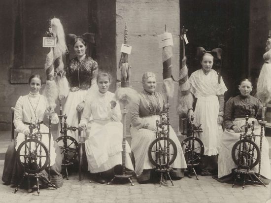 Frauen in badischer Tracht mit Spinnrädern.