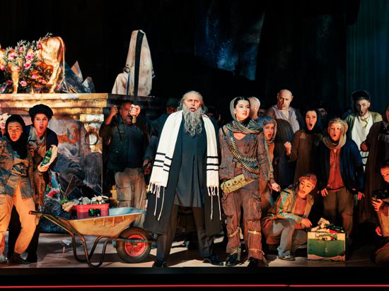 Szene aus der Oper „Nabucco“ am Staatstheater Karlsruhe 2023 mit dem Sänger Konstantin Gorny als Zaccaria, rechts neben ihm Aleksandra Domaschuk (Anna) sowie Mitglieder des Chores.