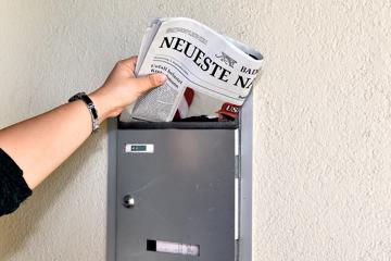 Eine Hand steckt eine Zeitung in einen Briefkasten.