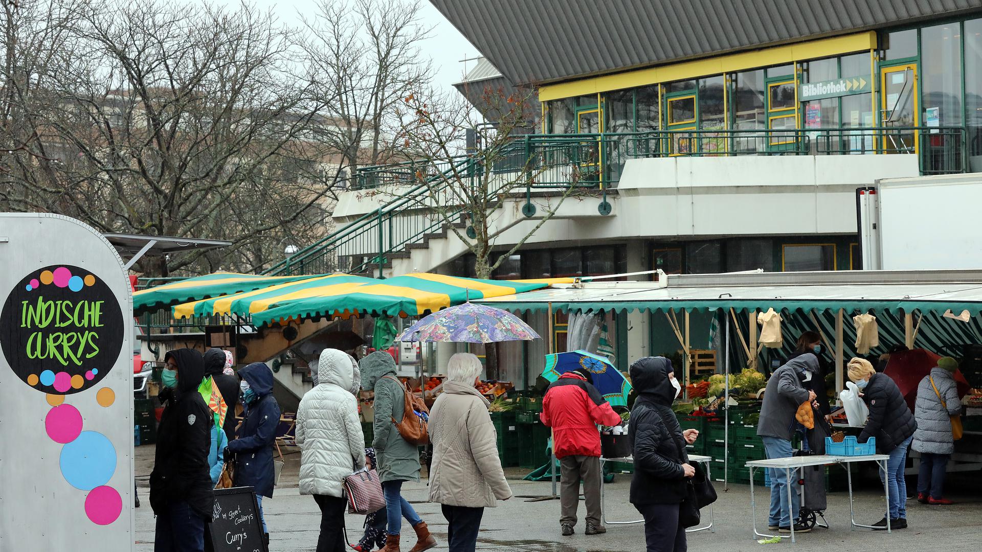 Menschen kaufen bei Regen auf dem Wochenmarkt in Neureut ein. 