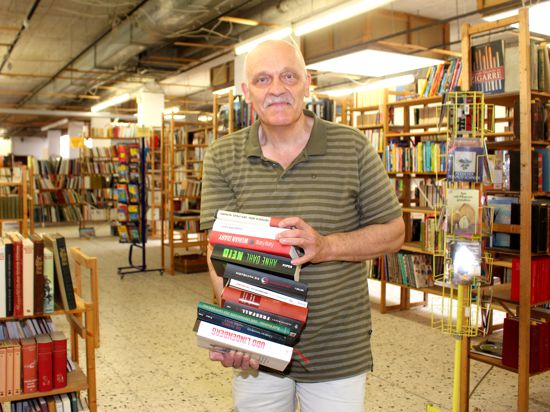 Thomas Stieber steht mit einem Bücherstapel auf dem Arm vor Bücherregalen