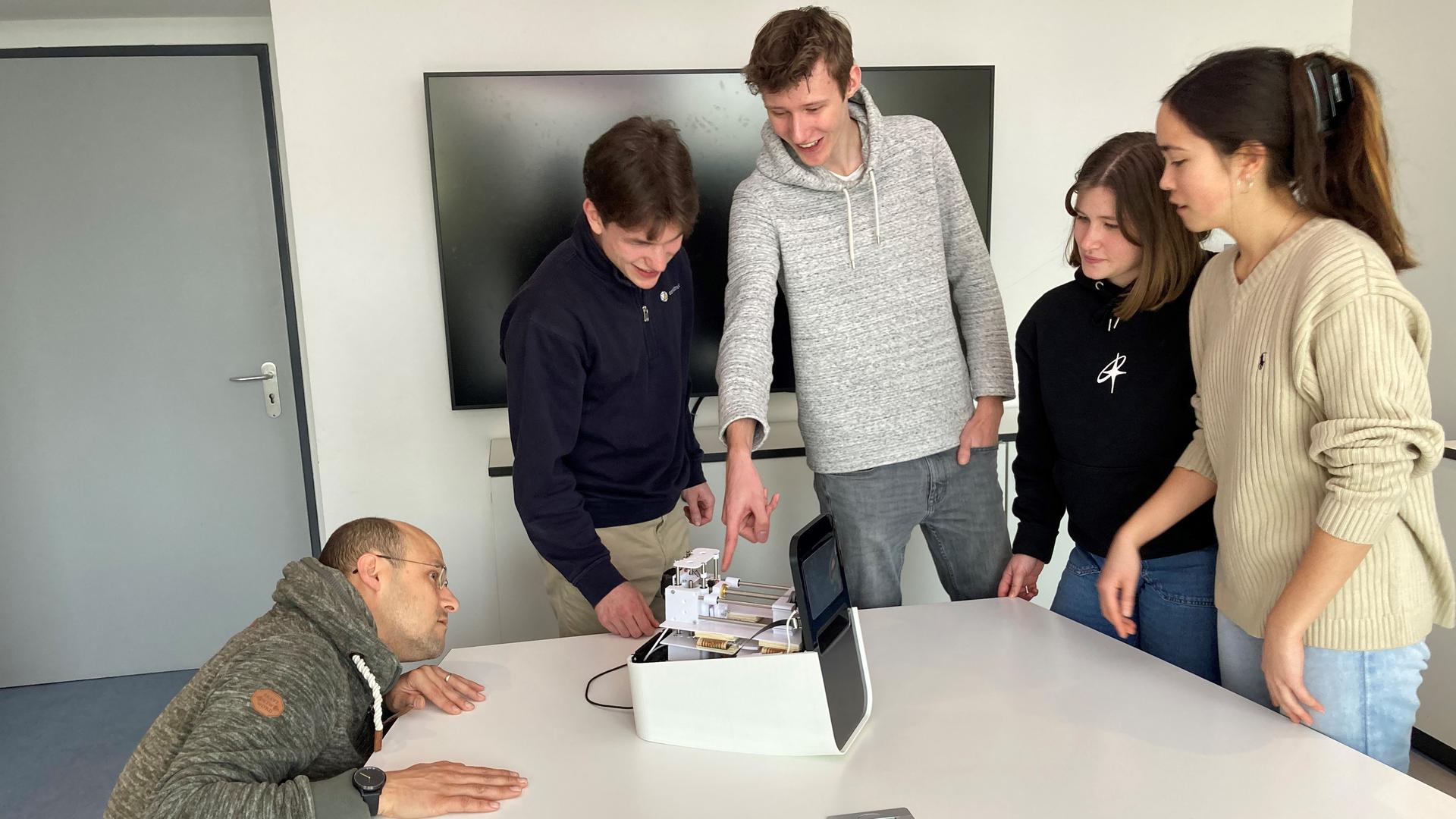 Dario Mager vom KIT lässt sich von den Studierenden Nicklas Rondot (von links), Leon Middendorf, Johanna Bartl und Alina Stein ihr PCR-Testgerät erklären.