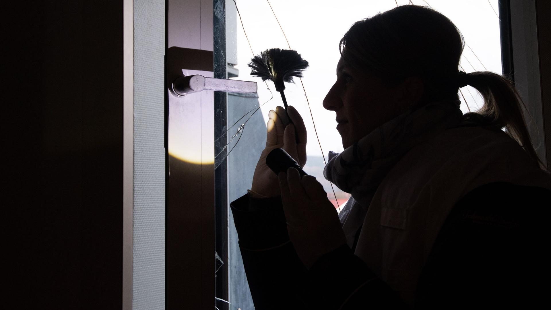 Eine Kriminaloberkommissarin  sichert nach einem Einbruch Spuren an einer eingeschlagenen Fensterscheibe.  