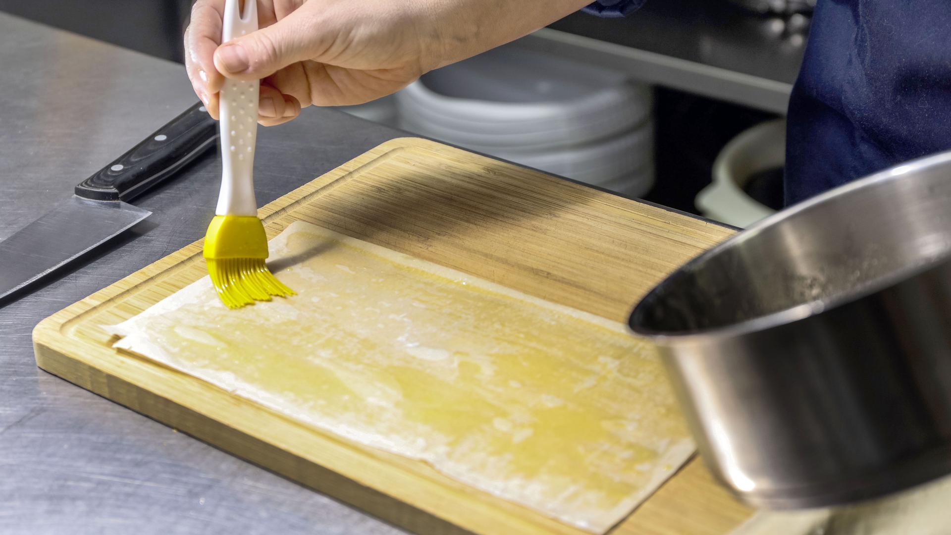 Ganze vier Platten des Filoteigs müssen dünn mit Butter bestrichen und übereinandergelegt werden. Die Platten werden anschließend in Quadrate geschnitten.