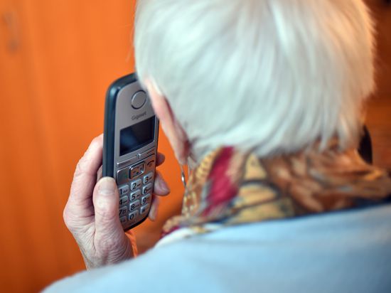 Eine Seniorin hält einen Telefonhörer an ihr Ohr 