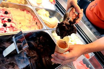 Die Inhaberin eines Eiscafés füllt mit einem Eisportionierer eine Waffel mit Schokoladeneis, das ohne Milchprodukte zubereitet wurde. 