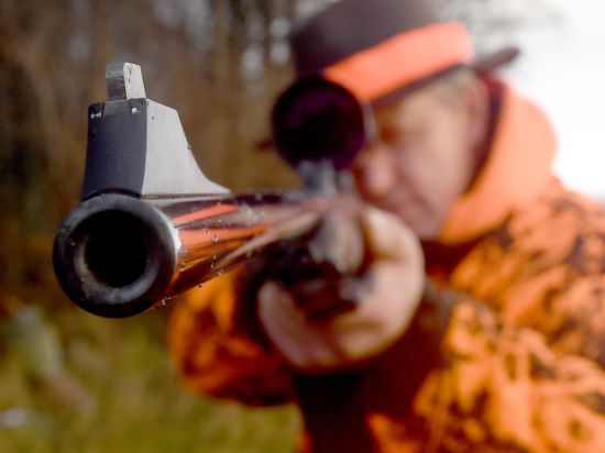 Ein Jäger steht mit dem Gewehr im Anschlag auf einem Feld.