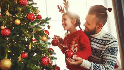 Ein Mann und ein kleines Mädchen schmücken einen Weihnachtsbaum. 