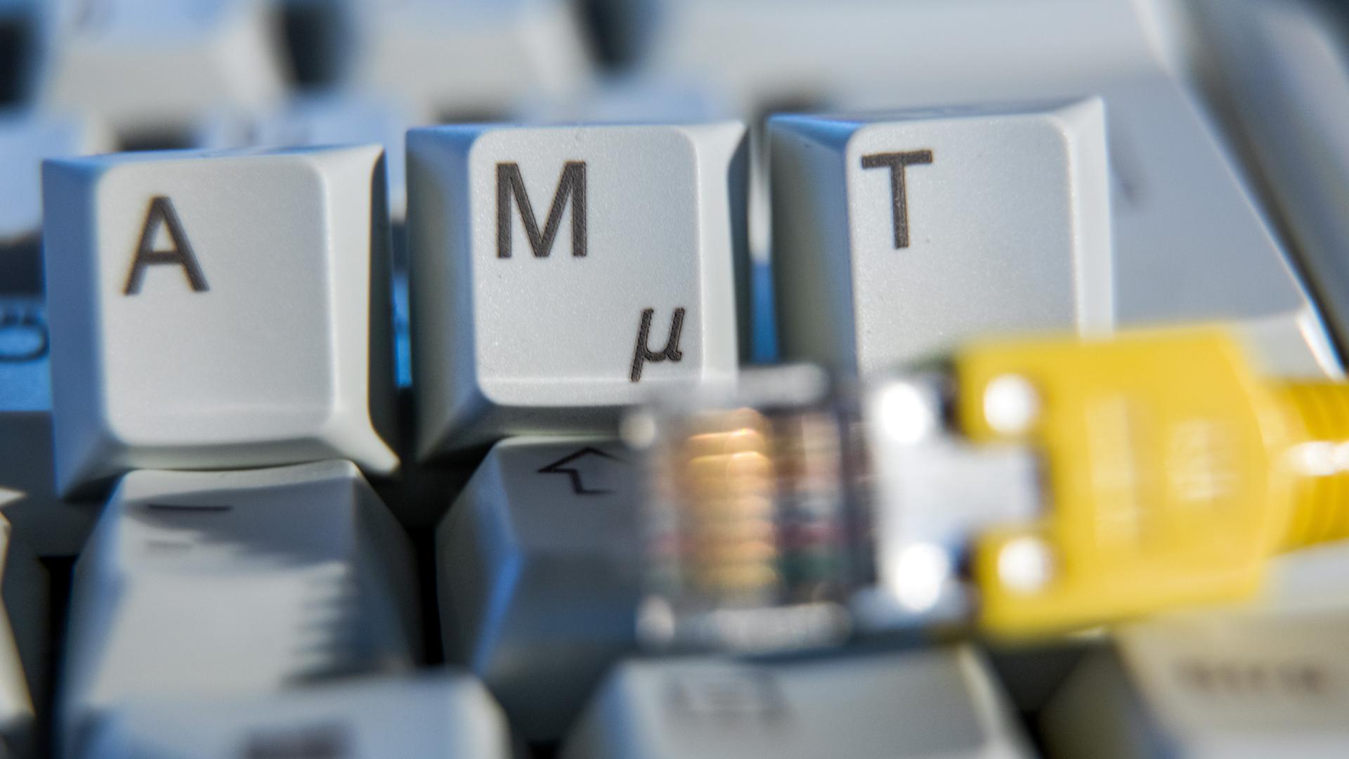 Der Schriftzug «Amt» ist auf einer Computertastatur hinter einem Netzwerkkabel zu sehen.