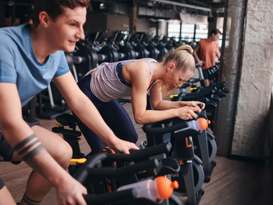 Ein junger Sportler und eine junge Sportlerin trainieren im Fitnessstudios auf dem Fahrraderometer.  
