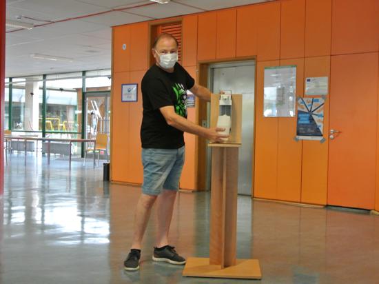 Ein Mann mit Maske steht neben einem Desinfektionsmittel-Spender