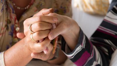 Eine Therapeutin  hält in einem Hospiz die Hand einer todkranken Bewohnerin.  
