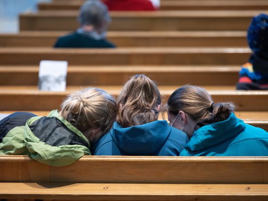 02.04.2021, Sachsen, Dresden: Junge Besucherinnen sitzen vor Beginn eines Karfreitag-Gottesdienstes in der Frauenkirche auf einer Kirchenbank nebeneinander. Foto: Sebastian Kahnert/dpa-Zentralbild/dpa +++ dpa-Bildfunk +++