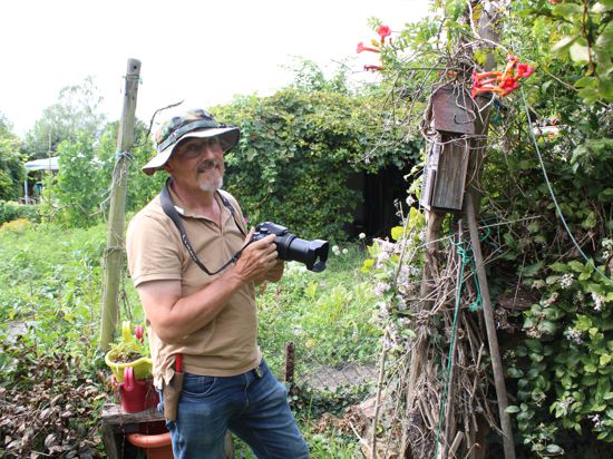 Ein Mann steht mit einer Fotokamera in seinem Garten.
