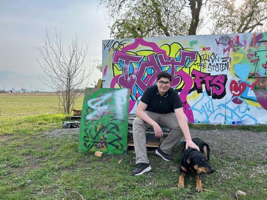 Jugendlicher sitzt mit Hund vor Graffiti-Mauer