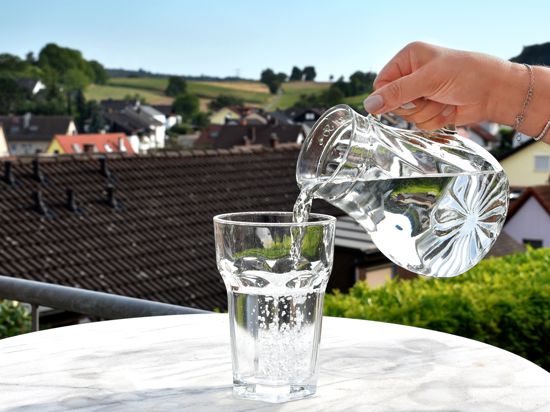 Person gießt Wasser aus einer Kanne in ein Glas.