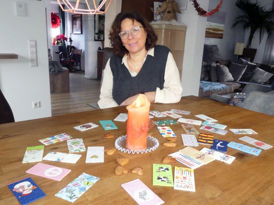 Frau sitzt an Tisch mit einer Kerze und vielen Karten