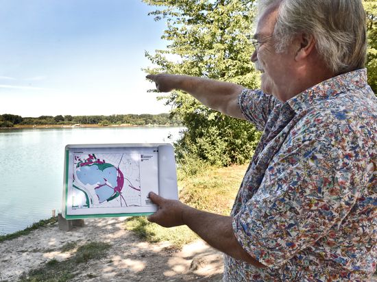Fritz Prosi zeigt mit einer Karte vor dem Baggersee Giesen, wie groß das Gewässer angelegt ist.