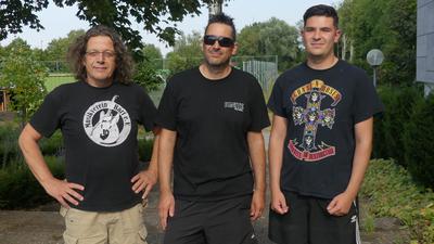 drei Männer in schwarzen T-Shirts stehen nebeneinander