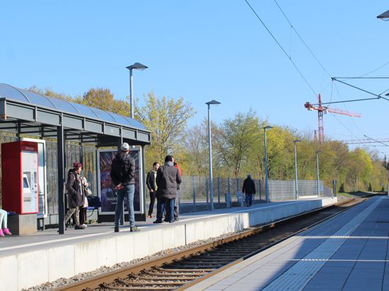 Menschen stehen an der Straßenbahnhaltestelle Leopoldstraße in Leopoldshafen. 