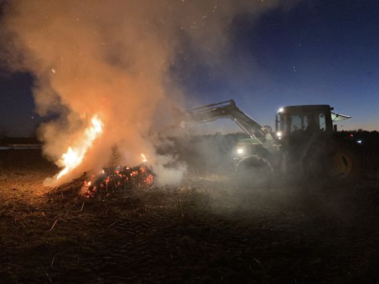 Ein Traktor schiebt brennendes Stroh auf einen Haufen.