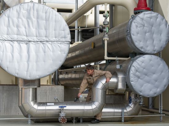  Ein Mitarbeiter steht  in einem Geothermiekraftwerk zwischen mehreren Behältern, die zum Austausch der Wärme genutzt werden.  