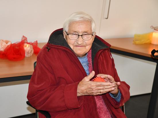 Die 90-jährige Gerda Seith sitzt auf einem Stuhl und rollt einen Noppenball in den Händen.