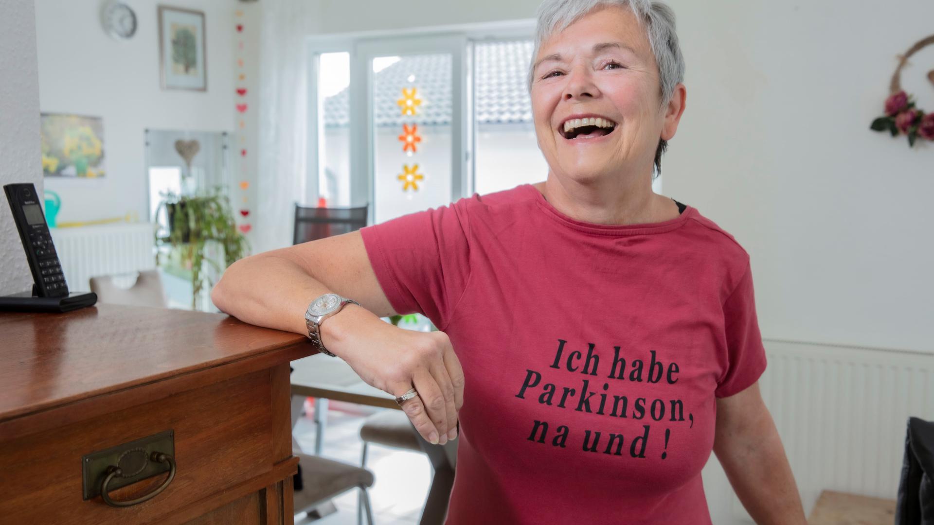 Iris Kraft steht mit Parkinson T-Shirt in ihrer Wohnung.