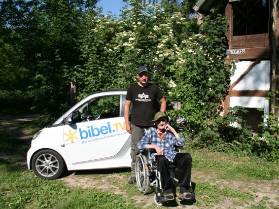 Olaf Stuckas sitzt im Rollstuhl auf einer Wiese. Marcel Kulz steht hinter ihm.