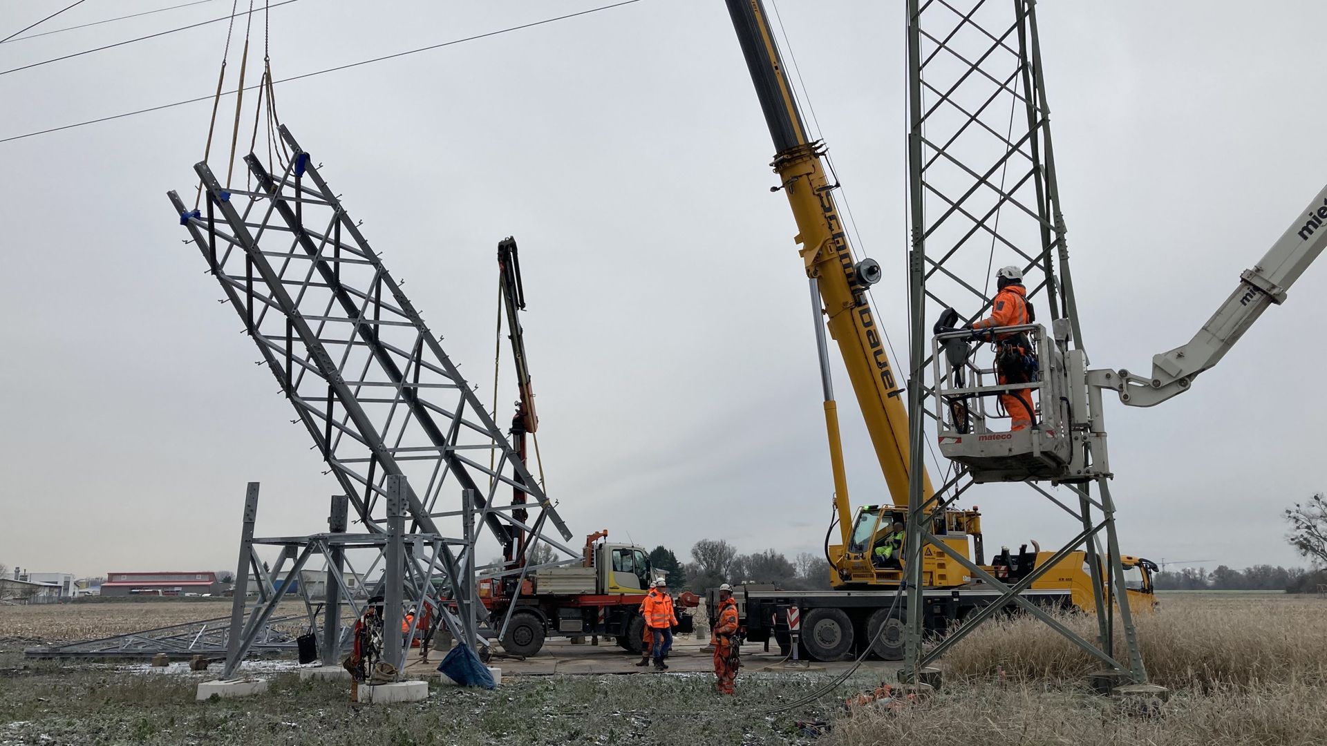 Arbeiter heben bei Hochstetten ein Bauelement für einen Strommast an einem Kran hoch. 