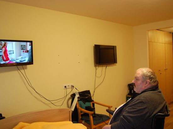 Uwe Bonrath sitzt in seinem Rollstuhl und guckt in einen Fernseher.