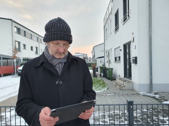 Achim Dittler steht vor Häusern und hat ein Tablet in der Hand. 