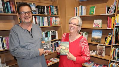 Andreas und Ingrid Mächtlinger stehen vor einem Bücherregal in der Bücheroase und halten jeweils ein Buch hoch. 